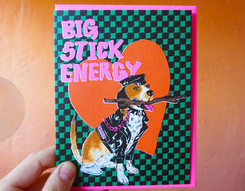 black and green checked background text reads big stick energy dog holding stick in mouth with red heart