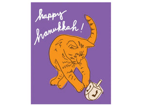 purple background, orange cat playing with dreidel, text reads happy hanukkah!