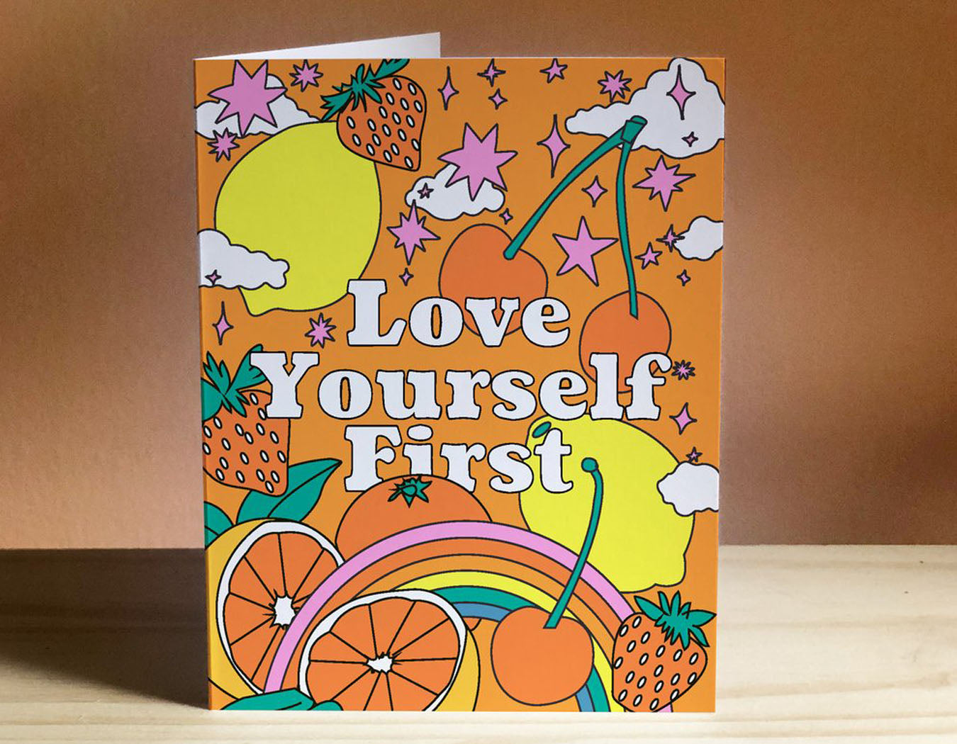 orange background strawberries lemons cherries rainbow stars clouds text reads love yourself first