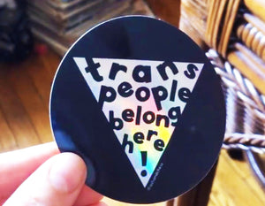 black circle sticker with text reads trans people belong here!